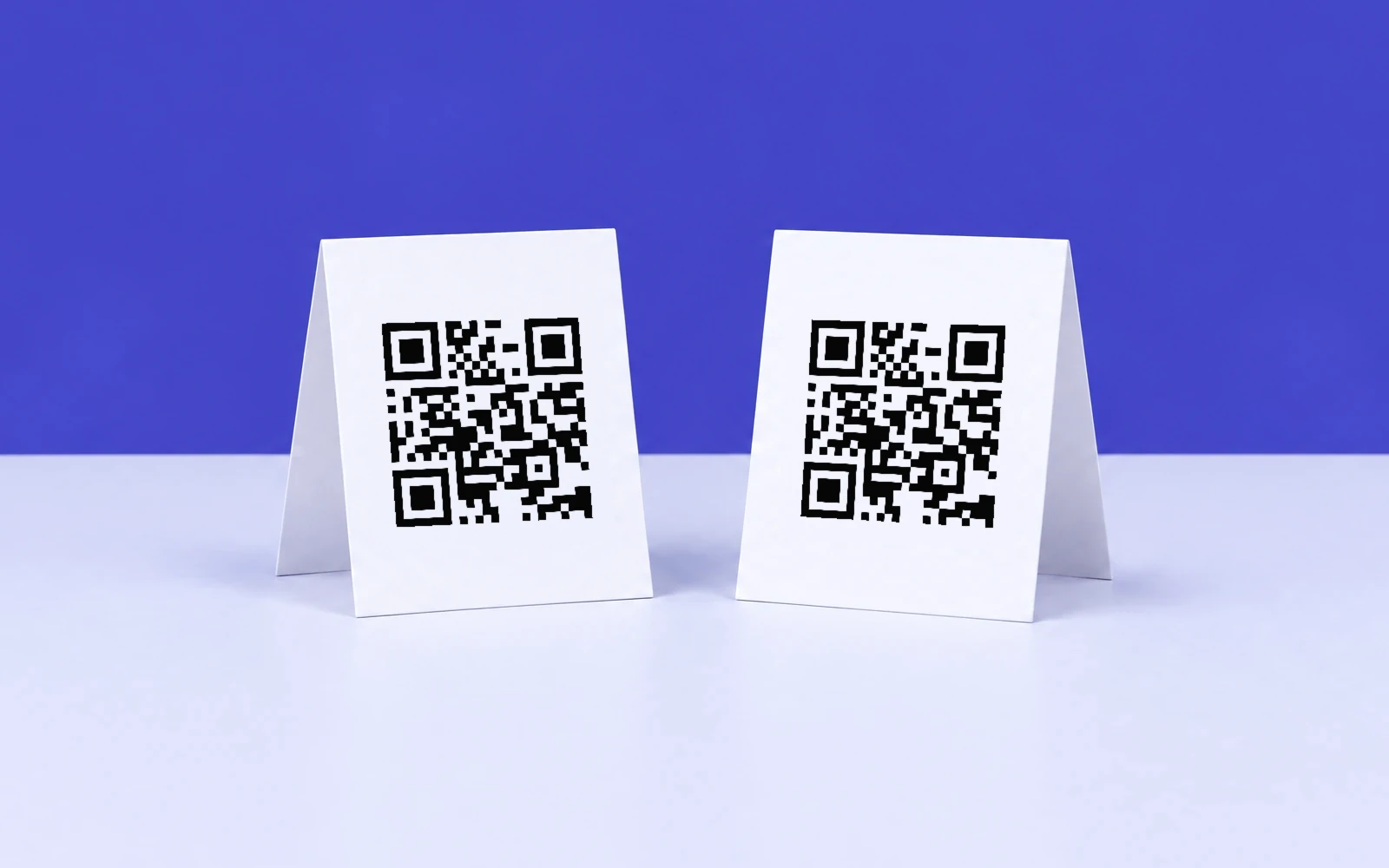 Deux chevalets blancs posés sur une table lavande pâle devant un mur indigo, chacun avec un QR code noir lisible qui mène à belentia.fr/outils.